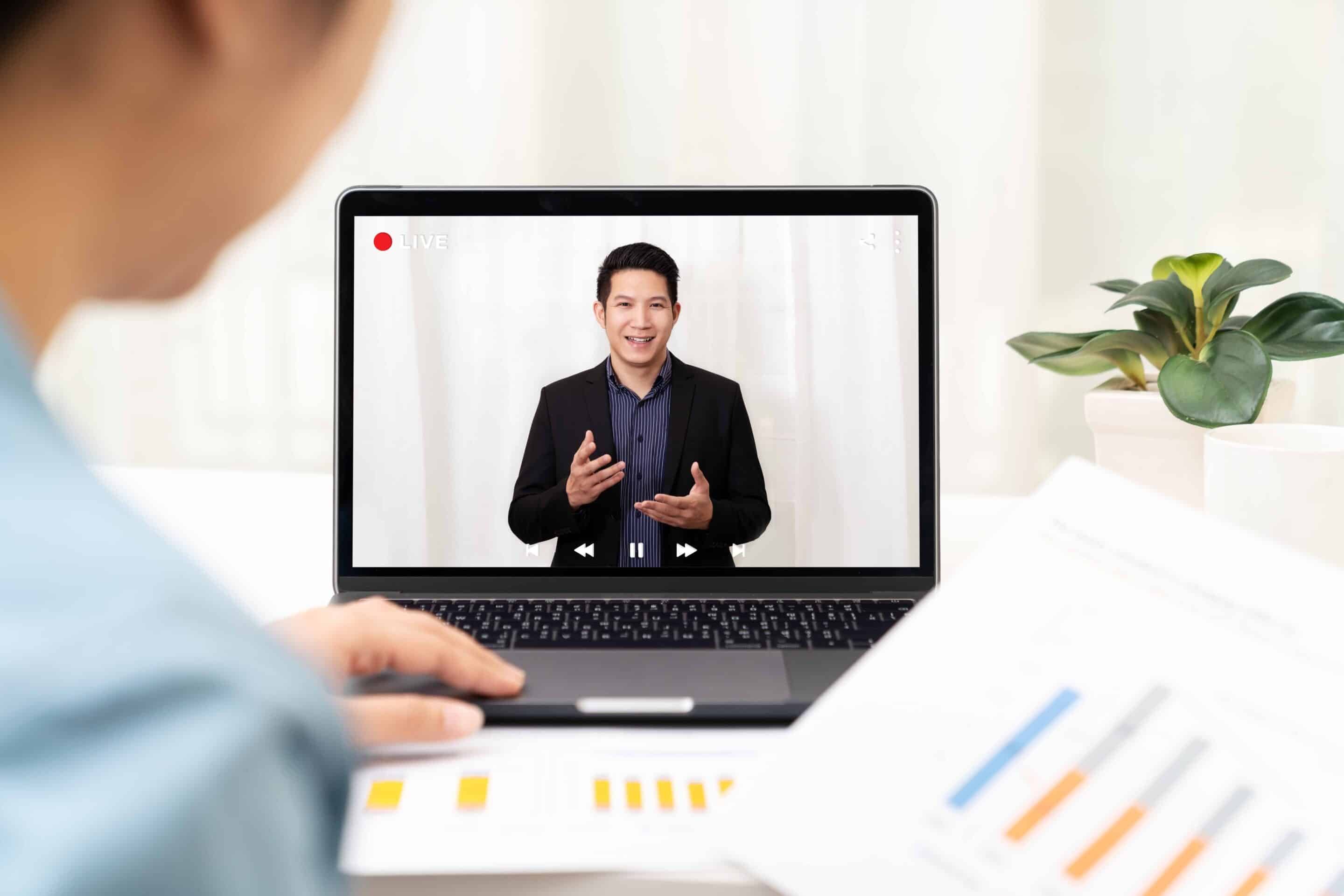 Business person watches Asian business leader host a broadcast-quality webcast on computer.